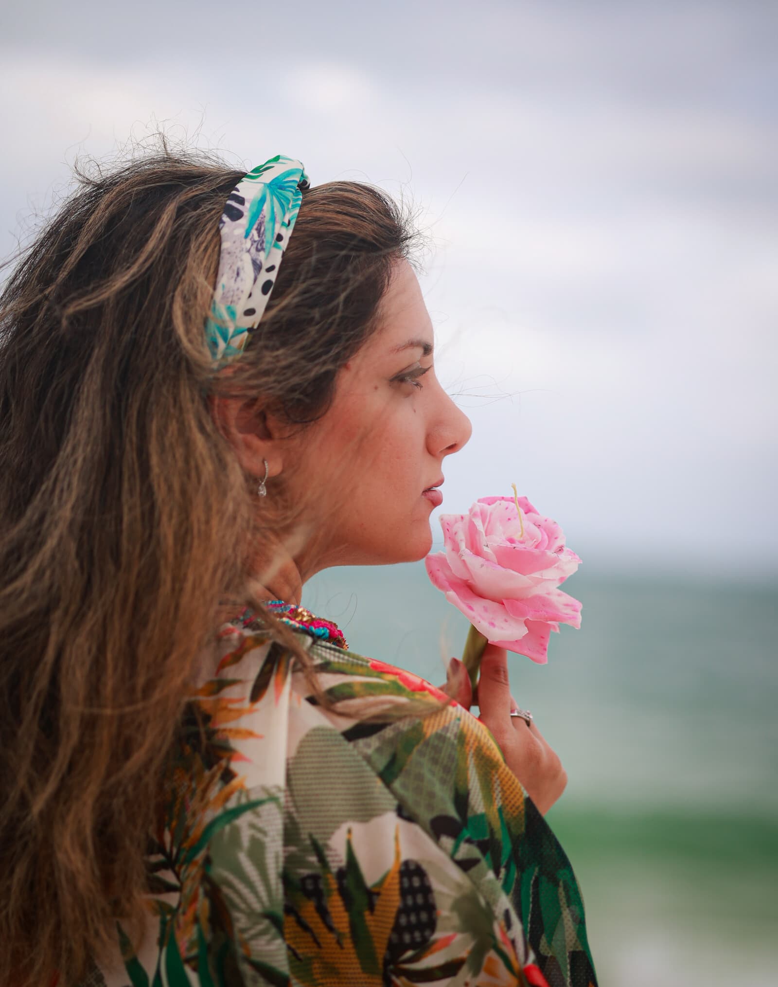 Nastaran holding a pink flower beside the water.
