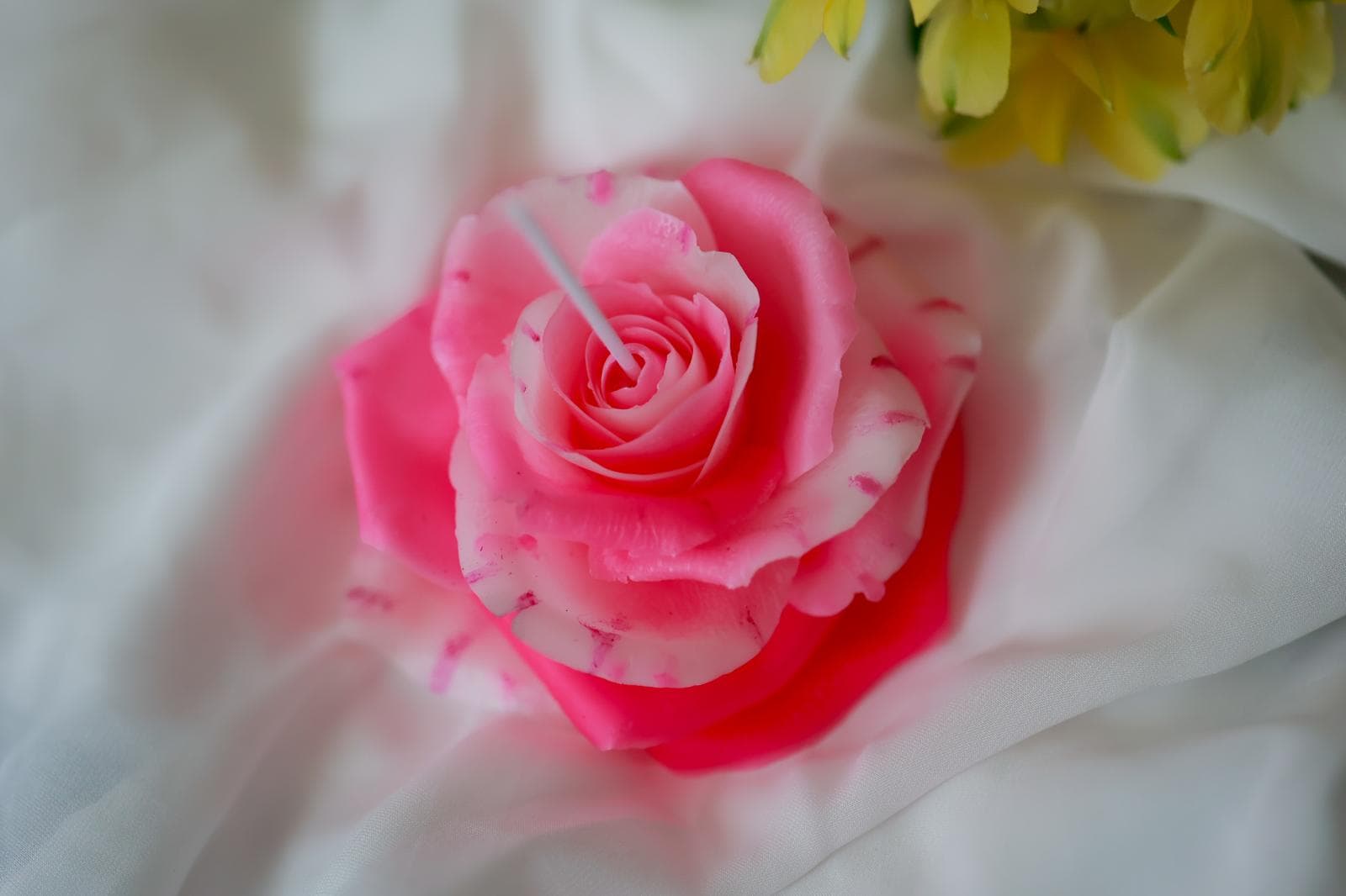 A close-up pink rose candle with a central wick.